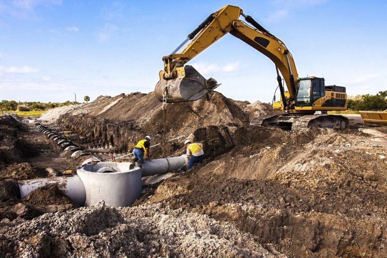 Excavator and crew laying new sewer pipe in an open trench